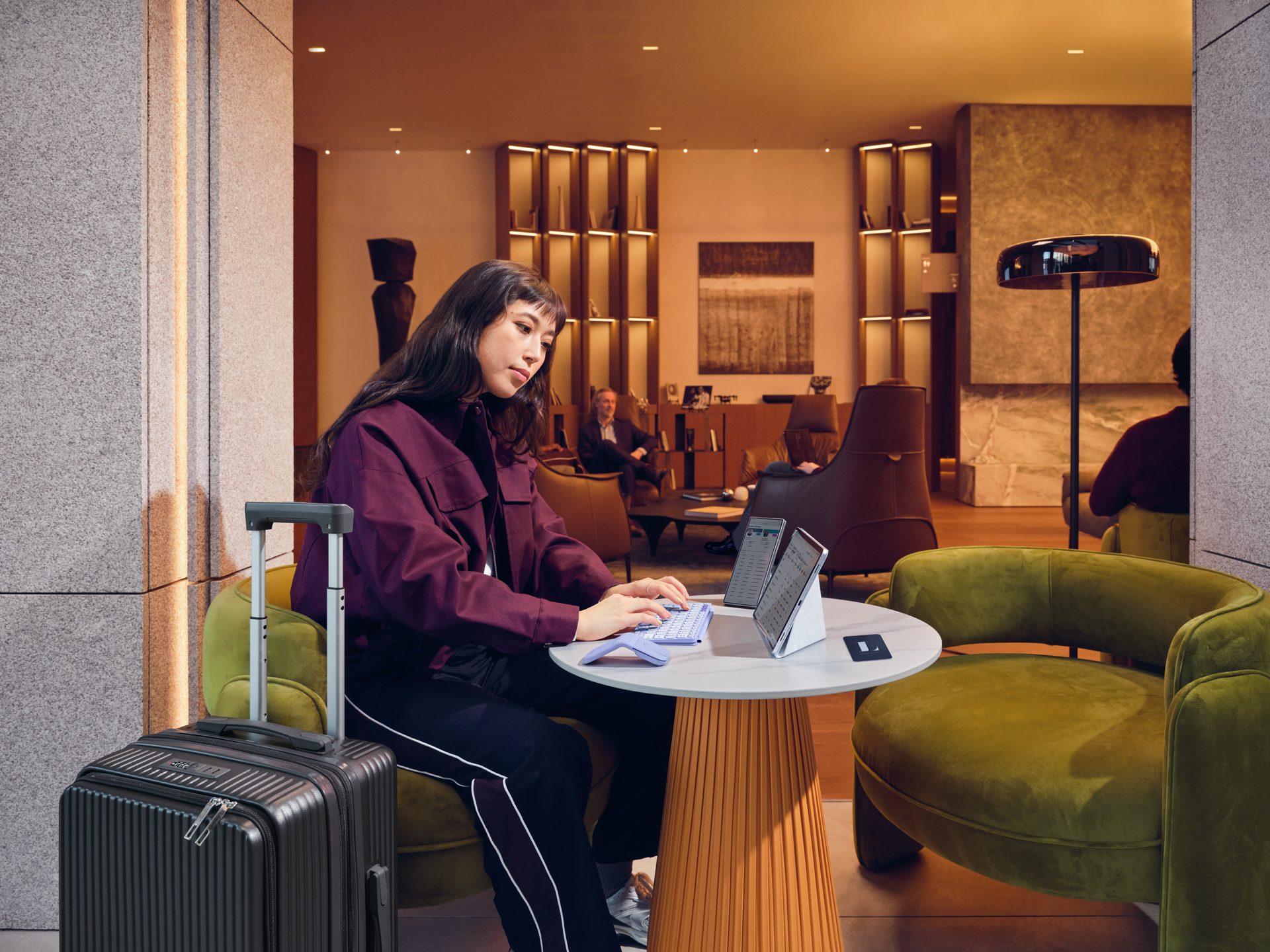 Woman working at a lounge table with a keyboard, mouse, and two tablets