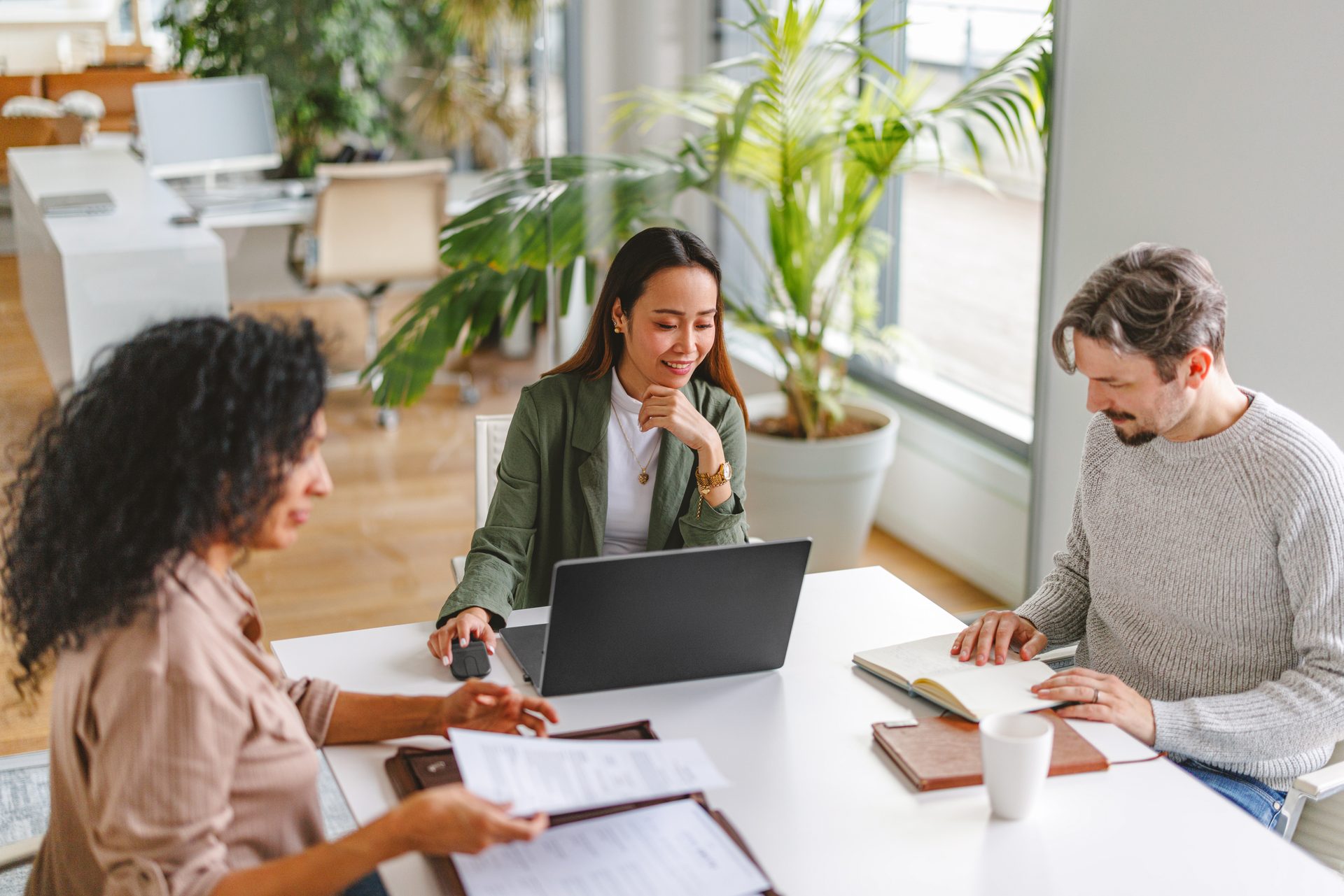 Three colleagues collaborating around a laptop in a bright office
