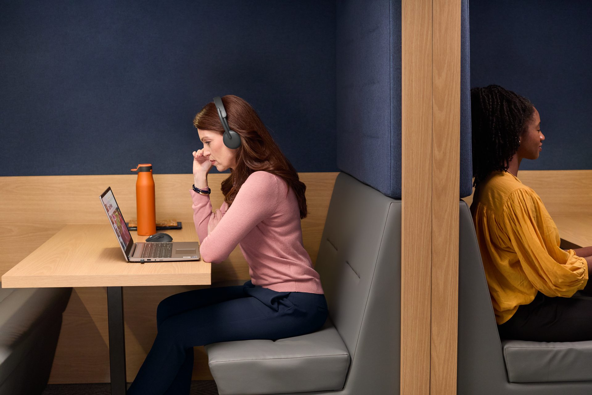 Two people working at desks separated by a wood and fabric partition